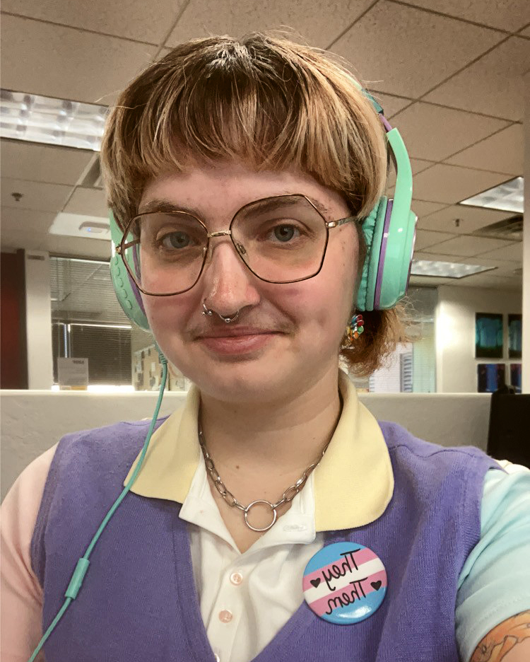 Person with blonde bangs wearing teal headphones, glasses, a yellow polo under a purple vest wearing a they/them button.